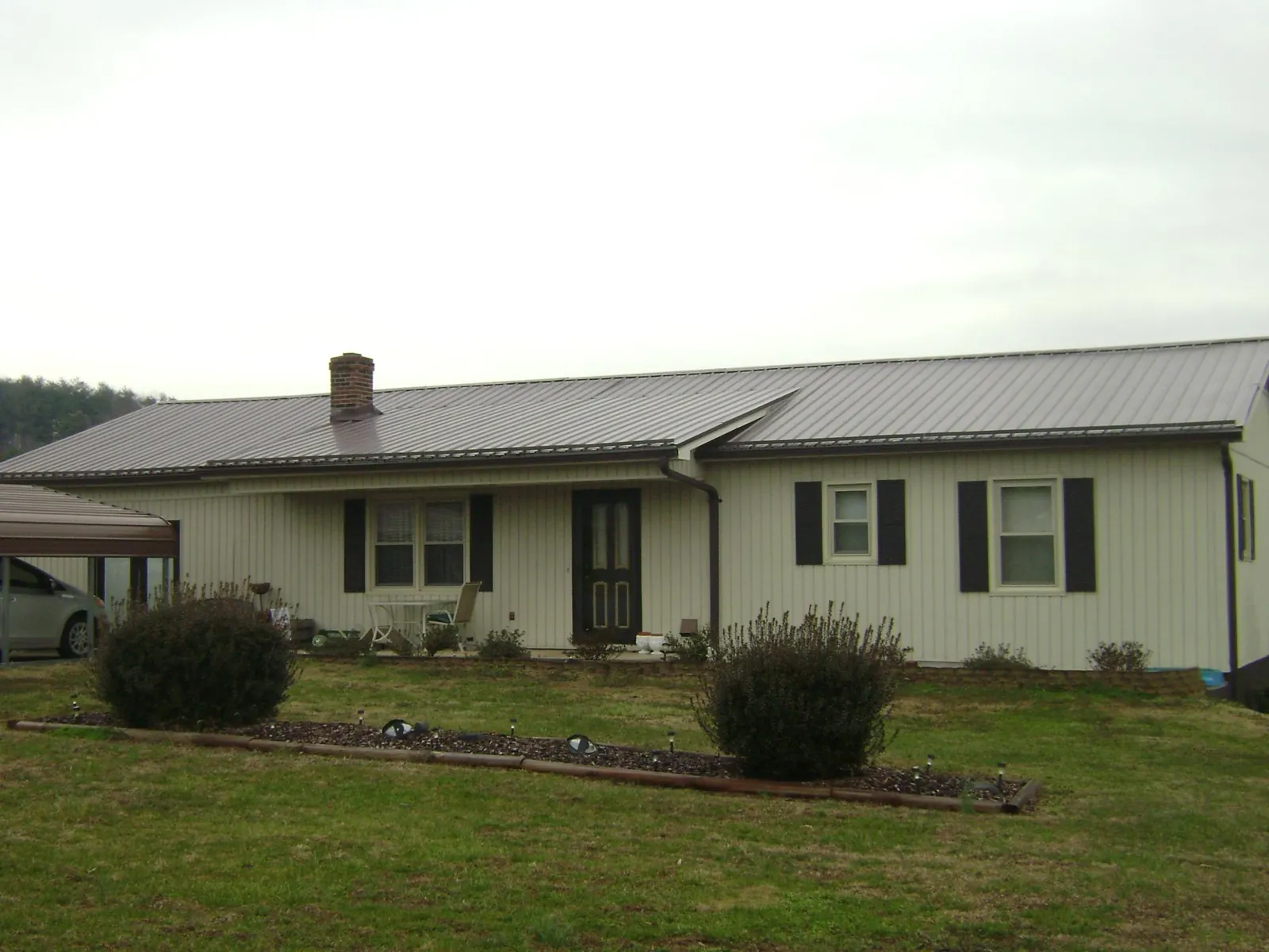 Brown metal roof on a cream sided ranch home with a brick chimney in Stafford